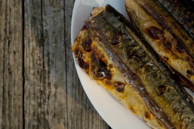 Close up of mackerel prepared on a grill in nature on a white plate. Selective focus. Top view. Wooden background.