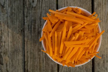 Bowl full of orange carrot sticks on wooden background. Close up. Selective focus. Top view.