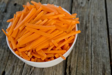 Bowl full of orange carrot sticks on wooden background. Close up. Selective focus.