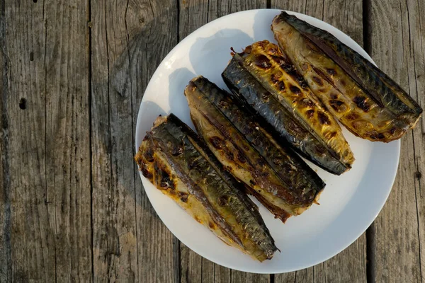 Four mackerel prepared on a grill in nature on a white plate. Selective focus. Top view. Wooden background.