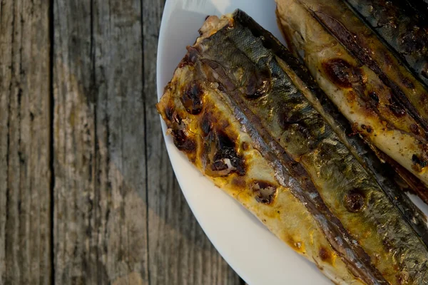 Close up of mackerel prepared on a grill in nature on a white plate. Selective focus. Top view. Wooden background.