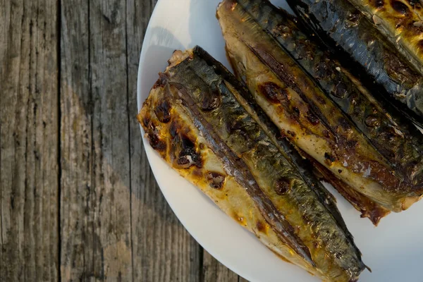 Close up of mackerel prepared on a grill in nature on a white plate. Selective focus. Top view. Wooden background.