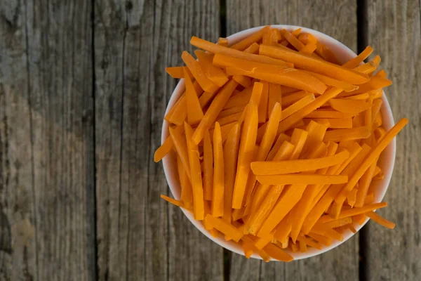 Bowl full of orange carrot sticks on wooden background. Close up. Selective focus. Top view.