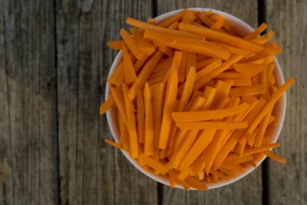 Bowl full of orange carrot sticks on wooden background. Close up. Selective focus. Top view.