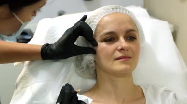 Beautician preparing woman's face for needle therapy treatment. Close-up. Slow motion.