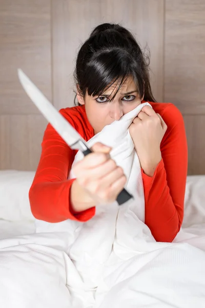 Mulher aterrorizada na cama segurando faca para autodefesa — Fotografia de Stock