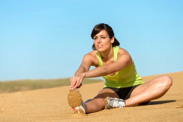 Athlete woman stretching leg on beach — Stock Photo, Image