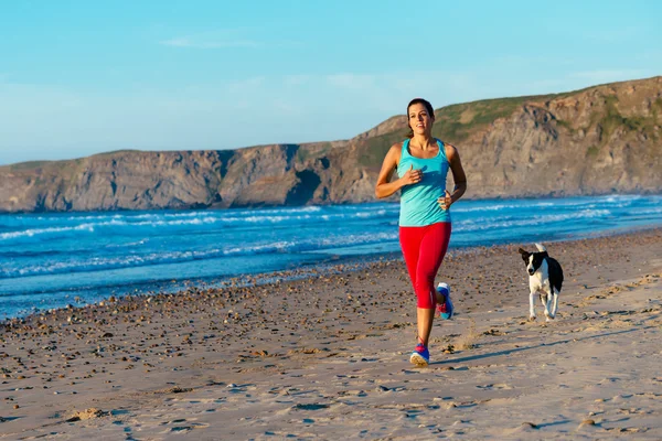 Фитнес-женщина и собака бегают по пляжу — стоковое фото