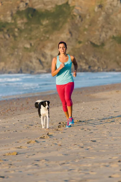 Sportig kvinna och hund kör på stranden — Stockfoto