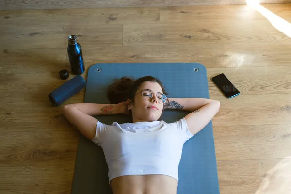 在家里做室内健身锻炼的时候 放松了的年轻健康女性正在休息 听着无线扬声器的音乐 — 图库照片