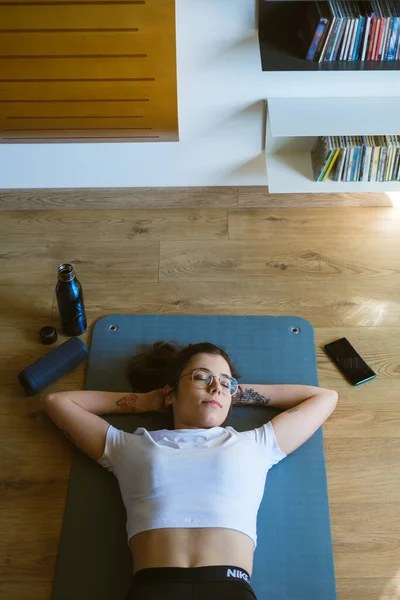 在家里做室内健身锻炼的时候 放松了的年轻健康女性正在休息 听着无线扬声器的音乐 — 图库照片