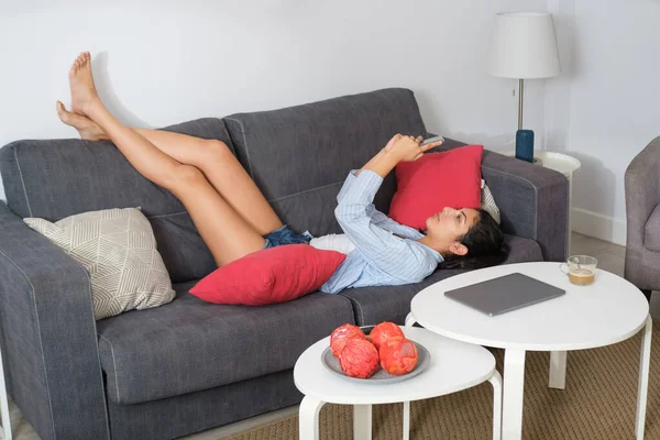 Relaxado Mulher Latina Casual Mensagens Texto Seu Smartphone Deitado Sofá — Fotografia de Stock