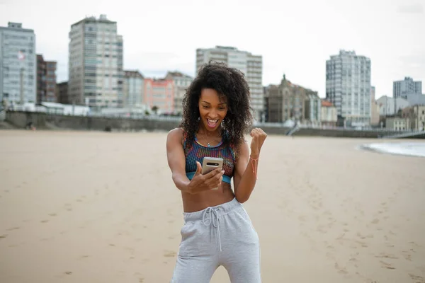 Young Urban Sporty Woman Celebrating Fitness Goals Success Using Smartphone lizenzfreie Stockfotos