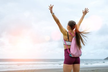 Fitness workout motivation and success. Sporty fit blissful woman celebrating training goals at the beach on sunset. clipart