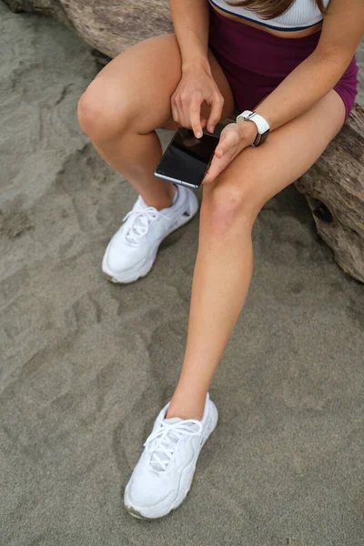 ビーチでトレーニングするためのフィットネスやランニング電話アプリを使用してフィットする女性アスリートの詳細 — ストック写真