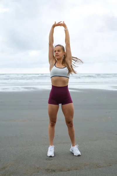 ビーチで働くスポーティな女性に合わせてください フィットネスと健康的なアウトドアライフスタイル 女性選手が腕と背中を伸ばしている スペインのアストゥリアス州海岸 — ストック写真