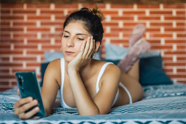 年轻的自然女人在家里放松 女人躺在床上用智能手机发短信 — 图库照片