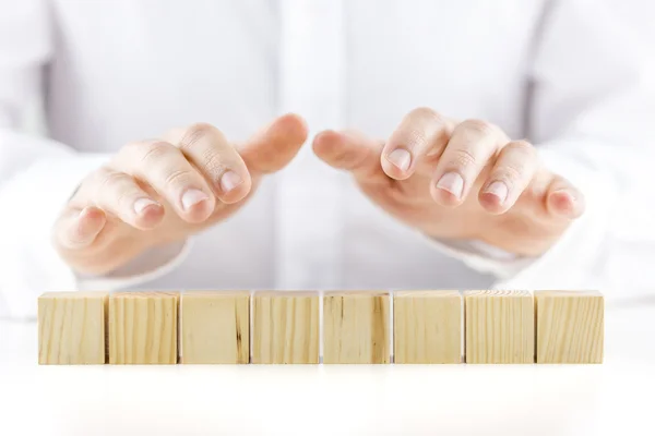 Uomo che tiene le mani protettive sopra otto cubi in legno — Stockfoto