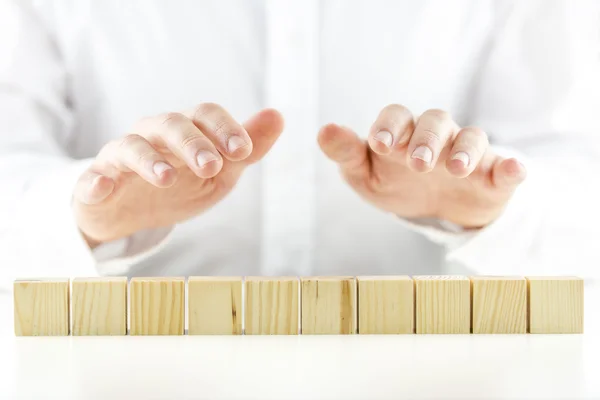 Man holding protective hands above ten wooden cubes — Stock Photo, Image