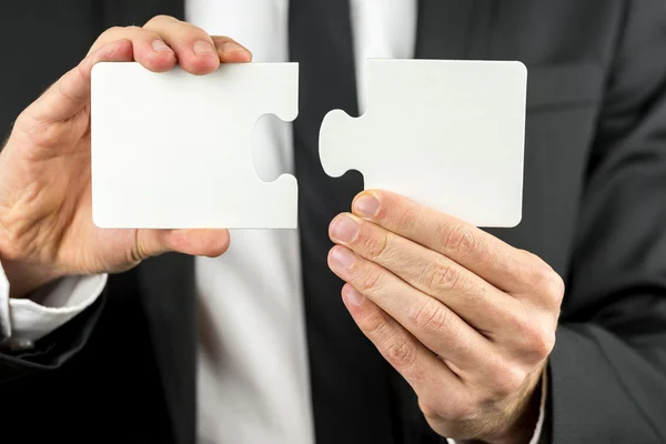 Empresário segurando duas peças de um quebra-cabeça em branco — Fotografia de Stock
