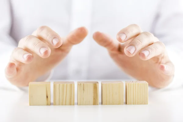 Hombre sosteniendo sus manos sobre cinco cubos de madera en blanco — Foto de Stock