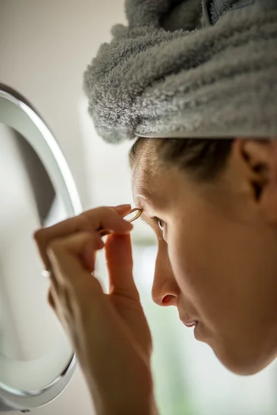 Vrouw plukken haar wenkbrauwen in de spiegel — Stockfoto