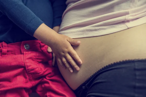 Criança segurando suas mães barriga grávida — Fotografia de Stock