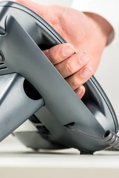 Hand picking up the receiver of a black telephone — Stock Photo, Image