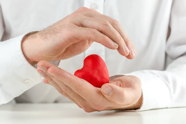 Zorgzame man cupping een rood hart in zijn handen — Stockfoto