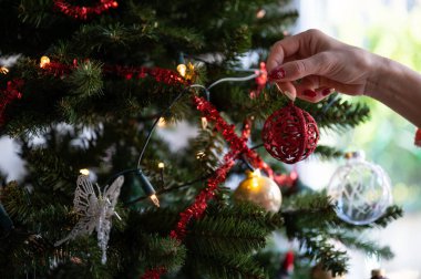 Kırmızı Holdiay manikürlü kadın eli Noel ağacını süslüyor, üzerinde parlak kırmızı bir mücevher asılı..
