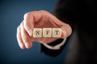 Closeup view of a businessman holding three dice in his hands spelling NFT.