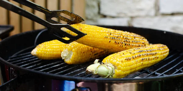 Turning corn on the cob grilling on backyard grill with a steel fork handles.