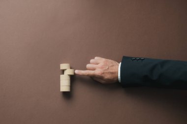 Hand of a businessman pushing a blank wooden cut circle into a stack of them  in a conceptual image. Top view over brown background.