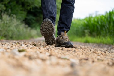 Low angle closeup view of a sole of male hiking shoes walking towards the camera on a gravel country road.