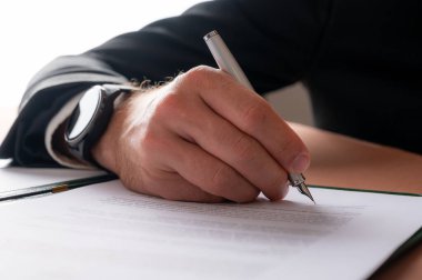 Low angle closeup view of a hand of a businessman with elegant watch on his wrist, signing a contract or document.