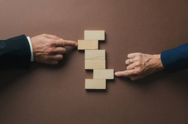 Business teamwork and partnership conceptual image - hands of a businessman and businesswoman pushing blank wooden pegs into a stack of others to create stability. 