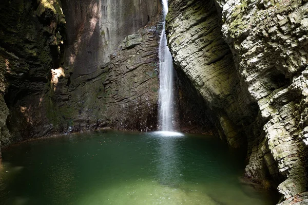 Beautiful waterfall kozjak falling into a green pool or lake surrounded by high rock cliffs.