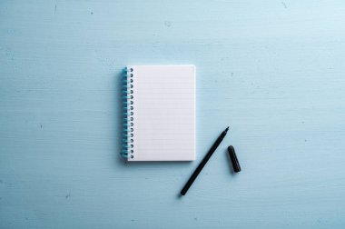 Top view of blank notepad with black marker placed on pastel blue wooden background.