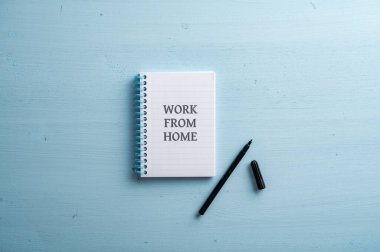 Üzerinde ev tabelası ve yanında mavi bir işaret olan spiral bir defter aç. Pastel mavi ahşap arka planda.