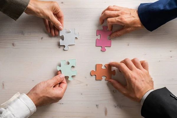 Four business people holding matching puzzle pieces of various pastel colours in a conceptual image of business teamwork and cooperation.