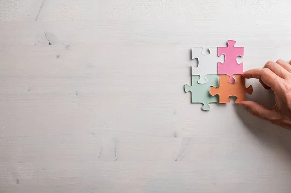 Mannelijke Hand Verbinden Van Vier Kleurrijke Puzzelstukjes Houten Achtergrond Met — Stockfoto