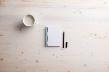 Boş spiral defter ve bir fincan taze kahve ile basit ahşap masa üzerine yerleştirilmiş siyah spiral kalem..