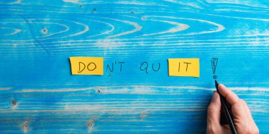 Male hand writing a Dont quit, Do it sign on bright yellow papers over aged blue wooden background.