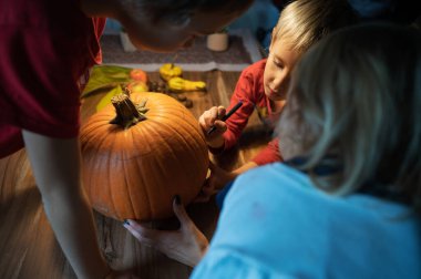 Üç çocuk, kardeşler, Cadılar Bayramı için oyacakları bir balkabağı çiziyorlar..