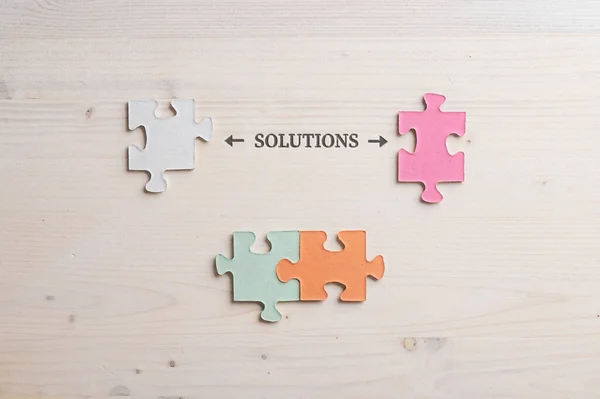 Conceptual image of problem solving with word Solution spelled over wooden background with four matching puzzle pieces around it.