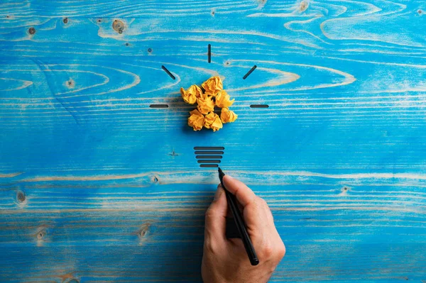 灯泡是由破碎的黄纸和男性手绘在能源和创新的概念形象基础上制成的 超薄的蓝色木制背景 — 图库照片