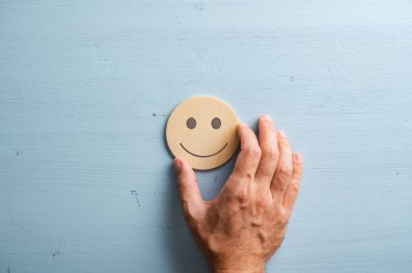 Erkek el, gülümseyen bir yüzü pastel mavi arka plan üzerinde ahşap bir kesim çemberine yerleştiriyor..