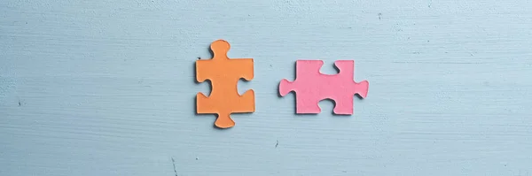 パステルブルーの木製の背景に配置された2つの空白のオレンジとピンクのマッチングパズルの作品のワイドビュー画像 — ストック写真