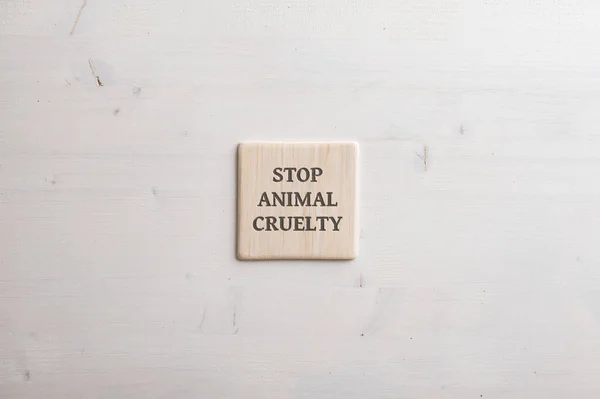 Wooden tile with a Stop animal cruelty sign on it placed over plain simple wooden background with copy space.