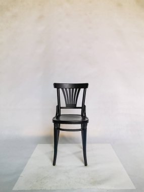 Beyaz duvarın önünde beyaz karton üzerinde duran tahta siyah sandalye. 